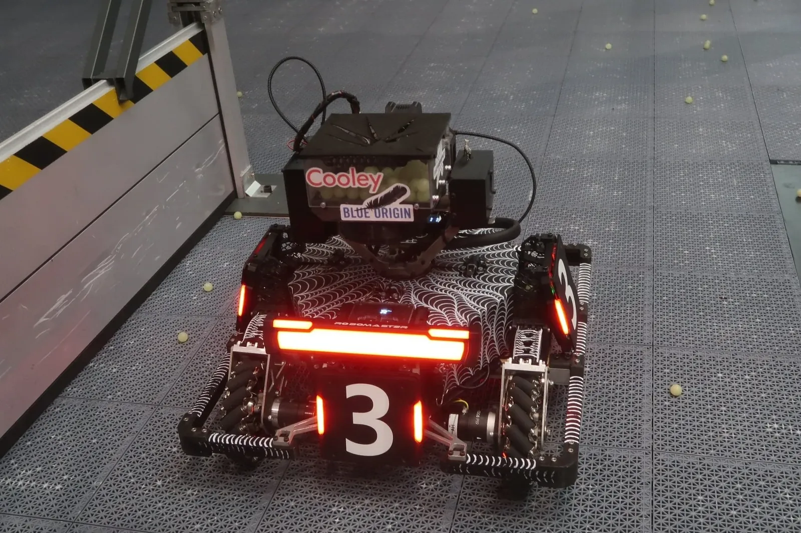 A robot numbered 3, red light bar lit, on a floor scattered with projectiles.